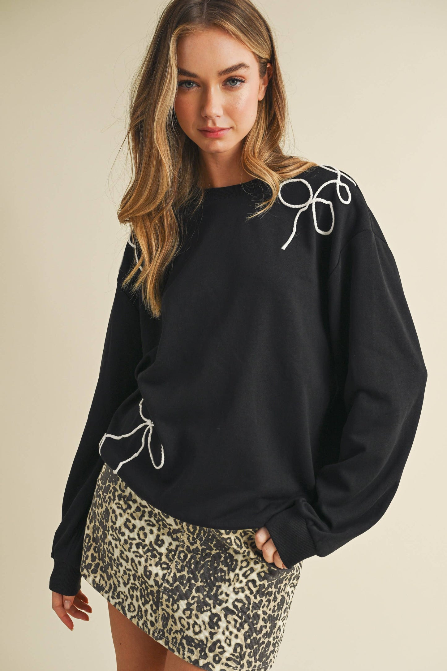 Woman wearing a black sweatshirt with white embroidery and a leopard print skirt on a beige background